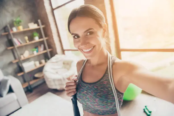 Close up portrait of excited active attractive cheerful beautiful strong skinny with beaming smile wearing sportive top with jump-rope on shoulders taking selfie for social-networks