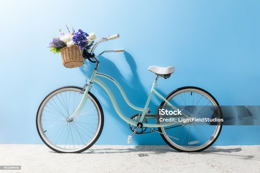 side view of bicycle with flowers in basket in front of blue wall Bicycle Stock Photo