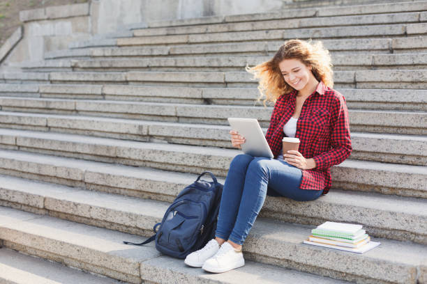 istock Student girl working on a tablet and drinking coffee outside 932289934