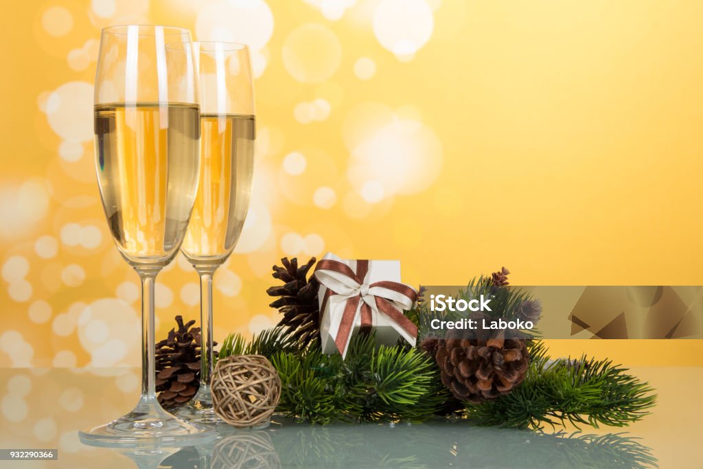 New Year pine branch with cones, gift and wine glasses with champagne, on yellow background New Year pine branch with cones, gift and wine glasses with champagne, on light yellow background Backgrounds Stock Photo