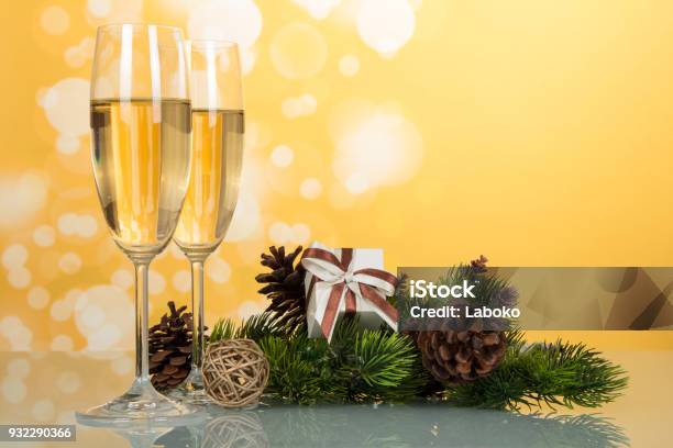 New Year Pine Branch With Cones Gift And Wine Glasses With Champagne On Yellow Background Stock Photo - Download Image Now