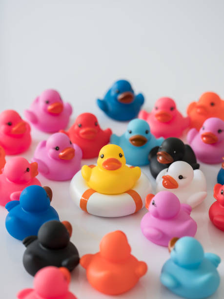 istock Yellow rubber duck on an inflatable life saving ring with many other colored ducks surrounding it. 932296656