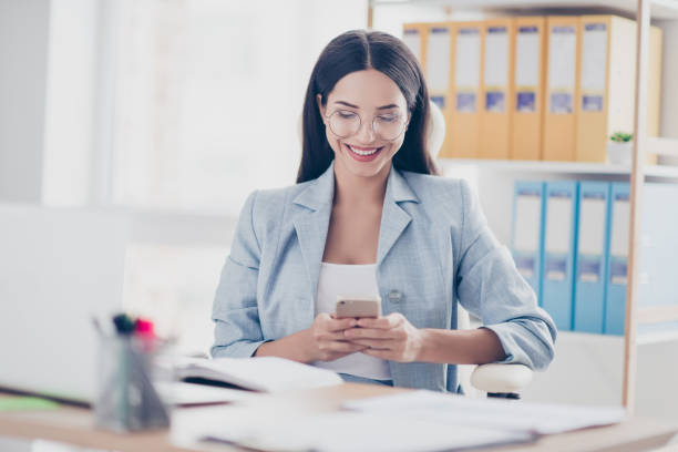 istock Pretty, charming, stylish, modern accountant in jacket using wi-fi, 3G internet on her smart phone, checking email,  sitting in desktop in work station 932302052