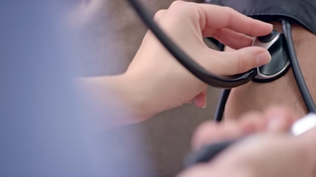 Nurse's hands measuring the patient's blood pressure while using a stethoscope on the patient's arm