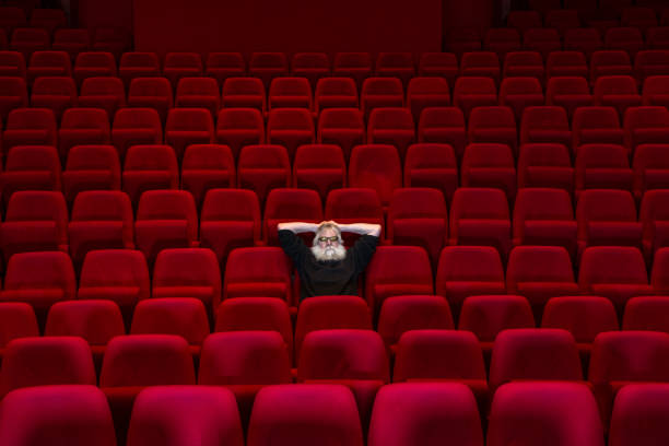 istock One man with white beard sits in Empty cinema or theatre with comfortable red seats 932311240