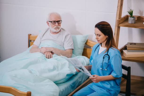 istock Old man patient looking at nurse reading newspaper 932321702