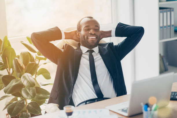 istock Attractive, cheerful, successful, stylish lawyer enjoying break time, having fun, holding hands behind the head, watching movie on laptop, sitting at desk in sun ray, beam, light, glare 932323474