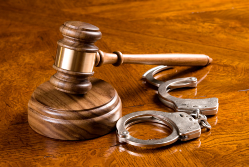 A gavel and block on a rich, cherry desktop with handcuffs.