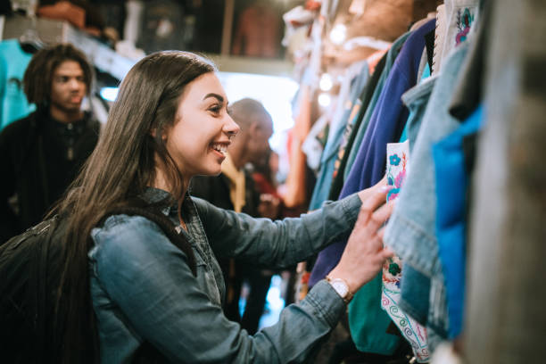 Young Adults Shop For Clothes at Thrift Store A smiling group of young adults have fun shopping for retro and vintage clothing styles at a second hand thrift store.  Mixed ethnic group.  Horizontal image with copy space. second hand stock pictures, royalty-free photos & images