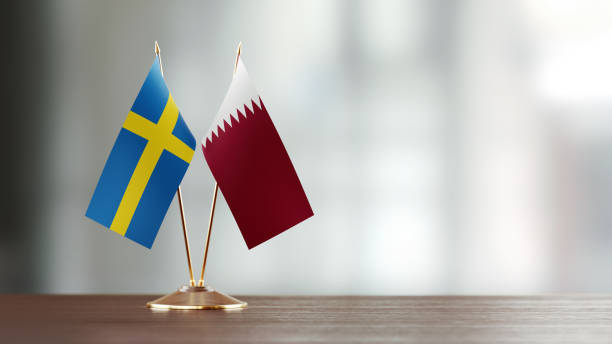 istock Swedish And Qatari Flag Pair On A Desk Over Defocused Background 932357594