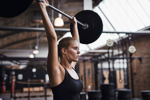 istock Young woman lifting weights over her head in a gym 932361894