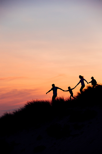 Silhouette of family running through the sand dunes at sunset.