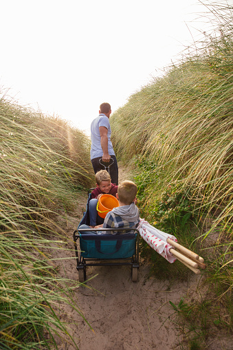 Rear view of father pulling a cart up a sand dune while his two children sit in the back.