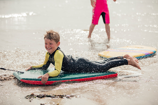 Little boy having fun at the beach, being pulled along on a body board.