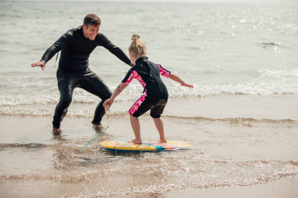 una niña de enseñanza cómo surf - surfing beach family father fotografías e imágenes de stock