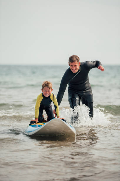 Watching his Son Learn how to Surf Little boy getting shown how to surf at the beach with his father. extreme dedication stock pictures, royalty-free photos & images