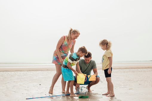 Family with two children looking through the buckets and fishing rods at the beach for sea life and shells.