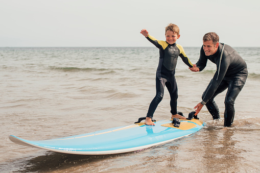 Little boy learning how to surf at the beach with his father.