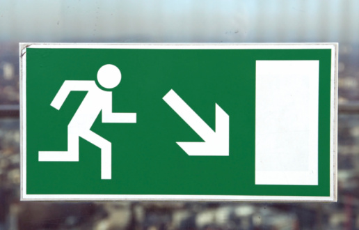 Emergency exit sign with an arrow in the direction to a door with another emergency exit sign. The sign is in a public building.