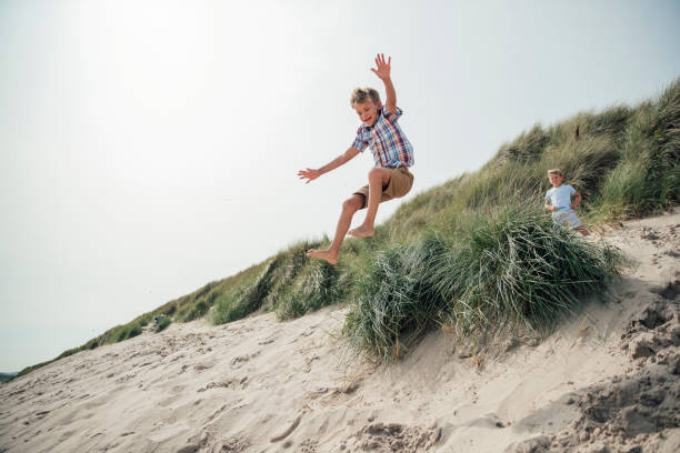 istock Little Boy Jumping Over a Sand Dune 932369966