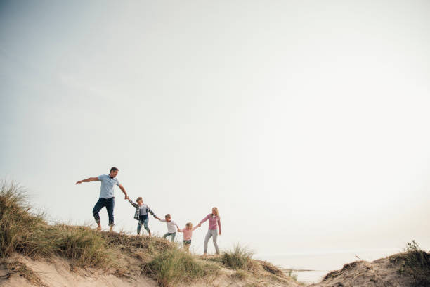 Exploring as a Family Family walking hand in hand along the top of a sand dune. Exploring the beach together. wide angle photos stock pictures, royalty-free photos & images