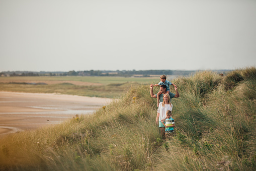 Wide angle view of a family walking through the sand dunes at the beach while on holiday.