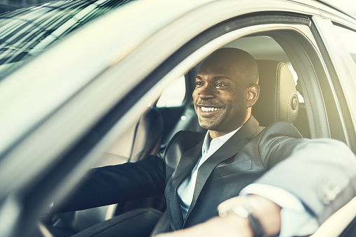 Young African businessman smiling while driving his car through the city during his morning commute to work