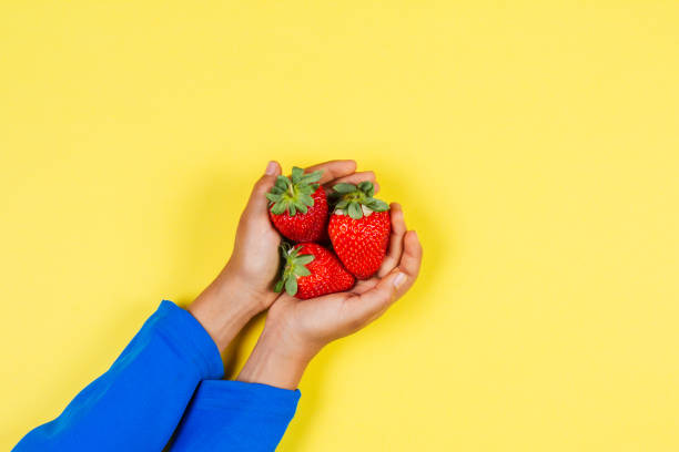 istock Kid hands holding fresh strawberries on yellow background 932384922