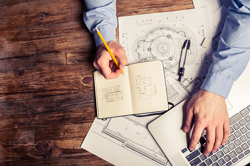 View from above of an Architect working at his desk. He is using the computer and hand drawn sketches to visualise the project.