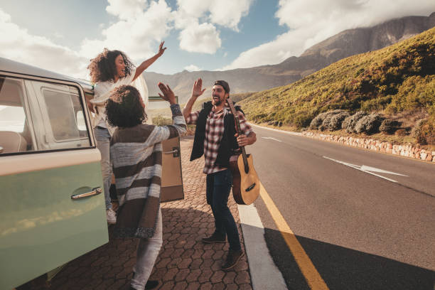 Group of man and women on road trip standing by the van and giving high five. Cheerful friends enjoying themselves on a vacation.