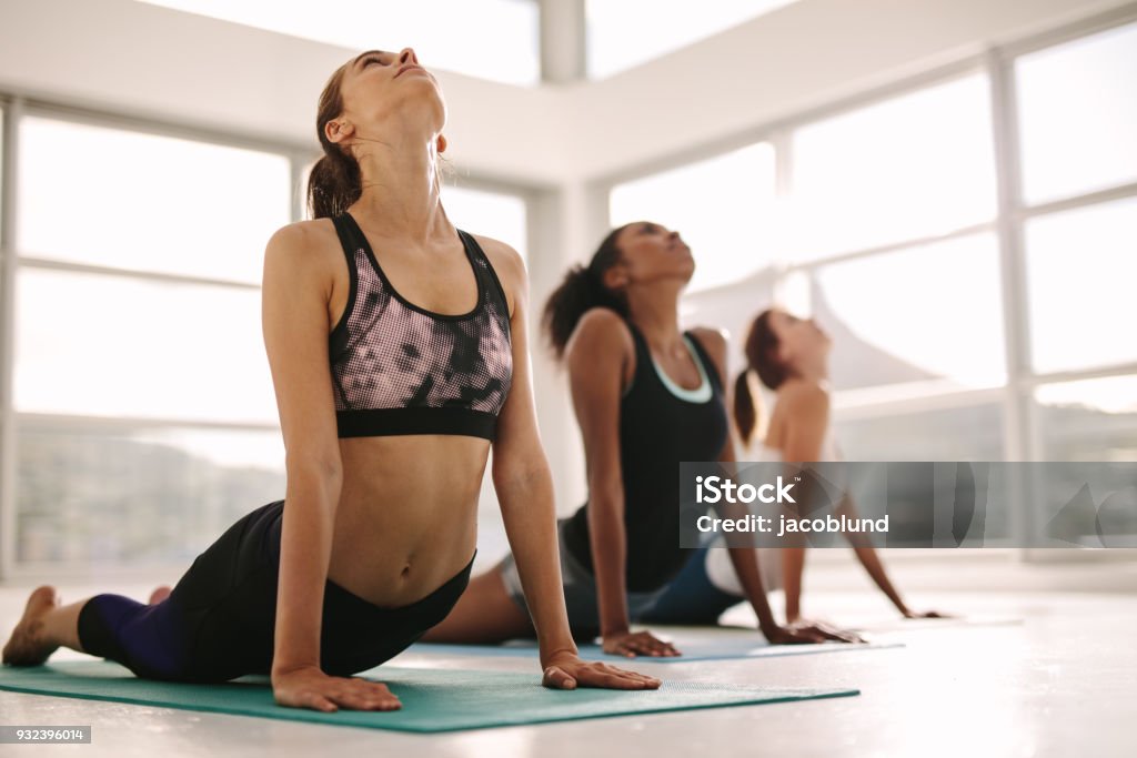 Women practicing yoga in fitness studio Young women practicing yoga. Fitness women meditating while doing cobra pose in gym. Yoga Class Stock Photo