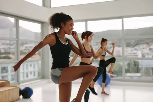 Multi ethnic group of women doing stretching exercises before intensive workout in spacious fitness studio. African female doing exercise with women in background.