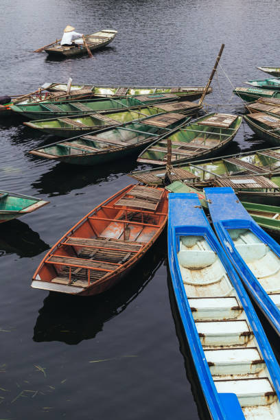 istock Empty rowing boats stop over the river with a man wearing white shirt and conical hat rowing boat in background at Trang An Grottoes in Ninh Binh, Vietnam. 932401720