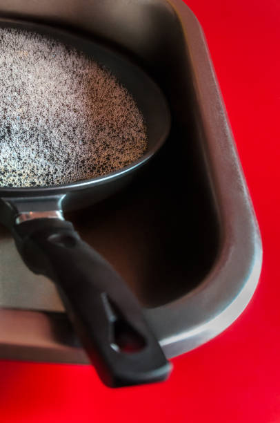 A dirty frying pan lying in a modern kitchen sink with dishwashing foam