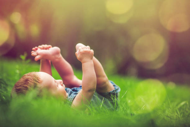 Cute baby playing with his legs on the grass Happy baby boy laying on the grass in summer Barefoot stock pictures, royalty-free photos & images