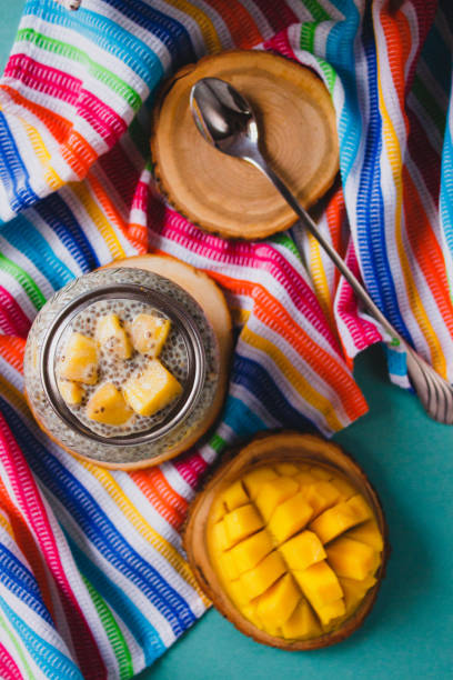 istock Chia pudding with yellow mango pieces on background of clorful striped kitchen cloth. Vegan healthy diet concept. 932420458