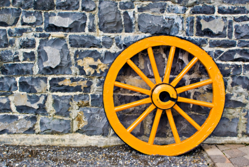 An old yellow wooden wagon wheel leaning against a stone wall