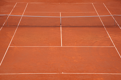 A yellow tennis ball and tennis racket lies on the clay court.