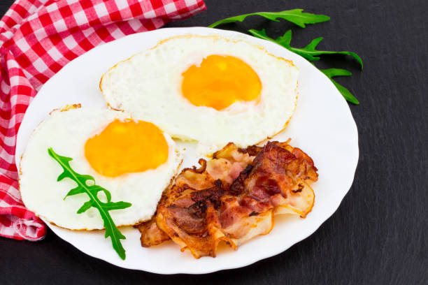 istock Breakfast with fried eggs, bacon and rucola salad on dark stone background 932433182