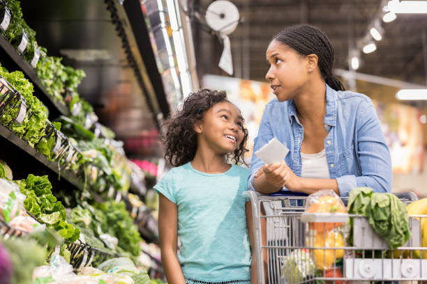 istock Cute girl talks with her mom while shopping for groceries 932439952