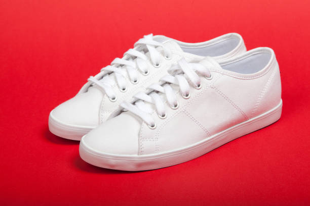 istock Pair of new white sneakers on red background 932444894