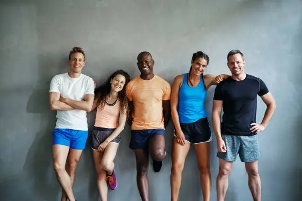 Smiling group of friends in sportswear laughing while standing arm in arm together in a gym after a workout