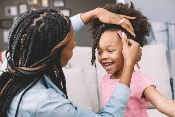 Little girl getting her hair twisted by her mom.