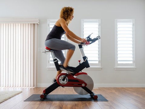 A woman exercising on a spin bike using an online instructor inside a home.