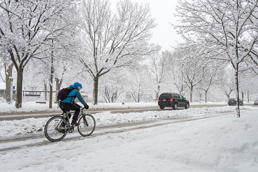 Montreal, CA - 14 March 2018: A man is riding a bicycle on a snowy street during snowstorm