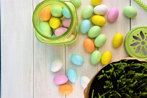 istock Green transparent glass jar with colored Easter eggs on the white wooden background 932463748