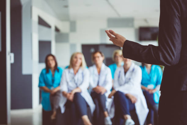 Woman giving a speech on seminar for doctors Sales representative giving a speech on seminar for doctors. Focus on woman’s hand. Defocused background. lecture hall training classroom presentation stock pictures, royalty-free photos & images