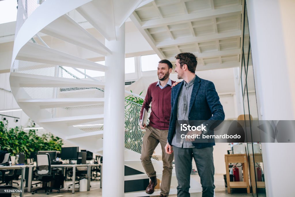 That was a great presentation Two businessman walking down the stairs in a modern office Hand On Shoulder Stock Photo