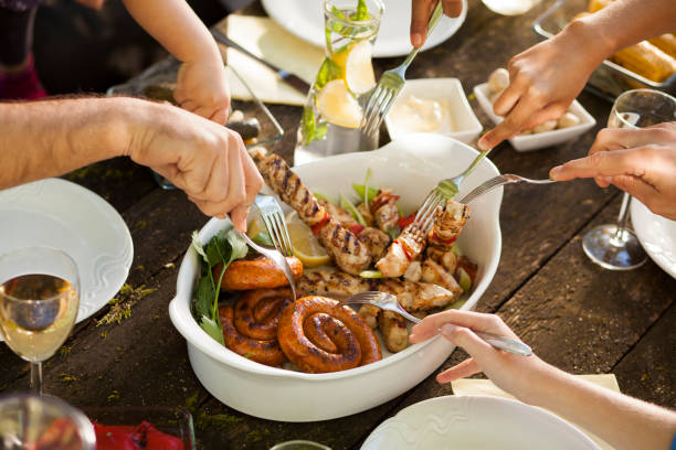 Family picnic table with bowl full of meet. Hands with forks taking meet.