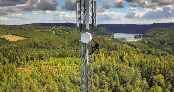Working at height Telecommunication manual high worker engineer installing new 4g, 5g LTE antenna on tall mobile base station (communication tower) in the middle of european forest. Working at height. Telecommunication masts and towers are typically tall structures designed to support antennas for telecommunications and broadcasting. Drone point of view. telecommunications equipment stock pictures, royalty-free photos & images